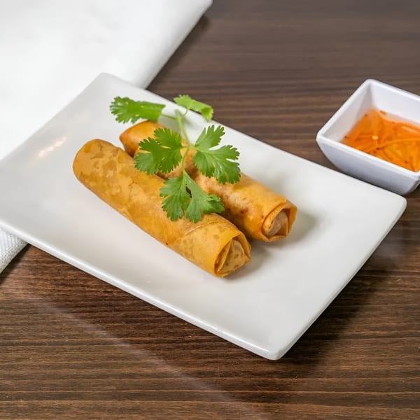 Two crispy golden spring rolls garnished with cilantro, served with a side of dipping sauce.