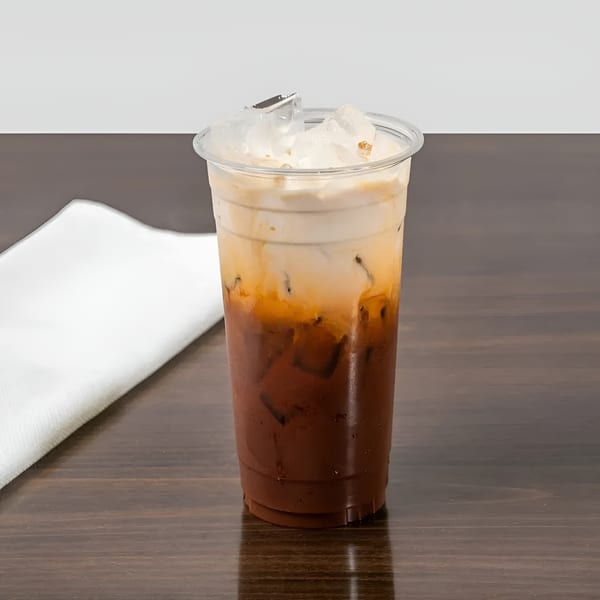 Iced Thai tea with milk and ice in a clear plastic cup on a wooden table.