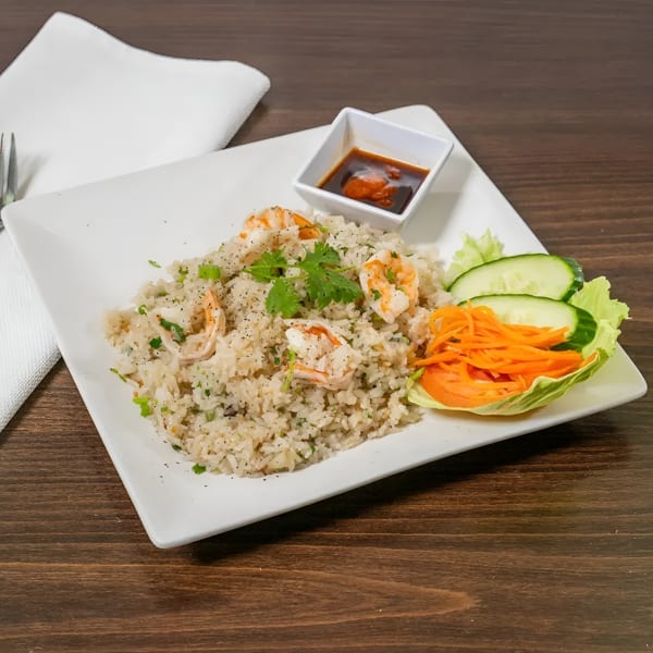 Shrimp fried rice with cilantro, green onions, and black pepper, served with a side salad and sauce.