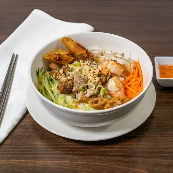 A Vietnamese vermicelli bowl with shrimp, pork, egg rolls, and vegetables, served with sauce.